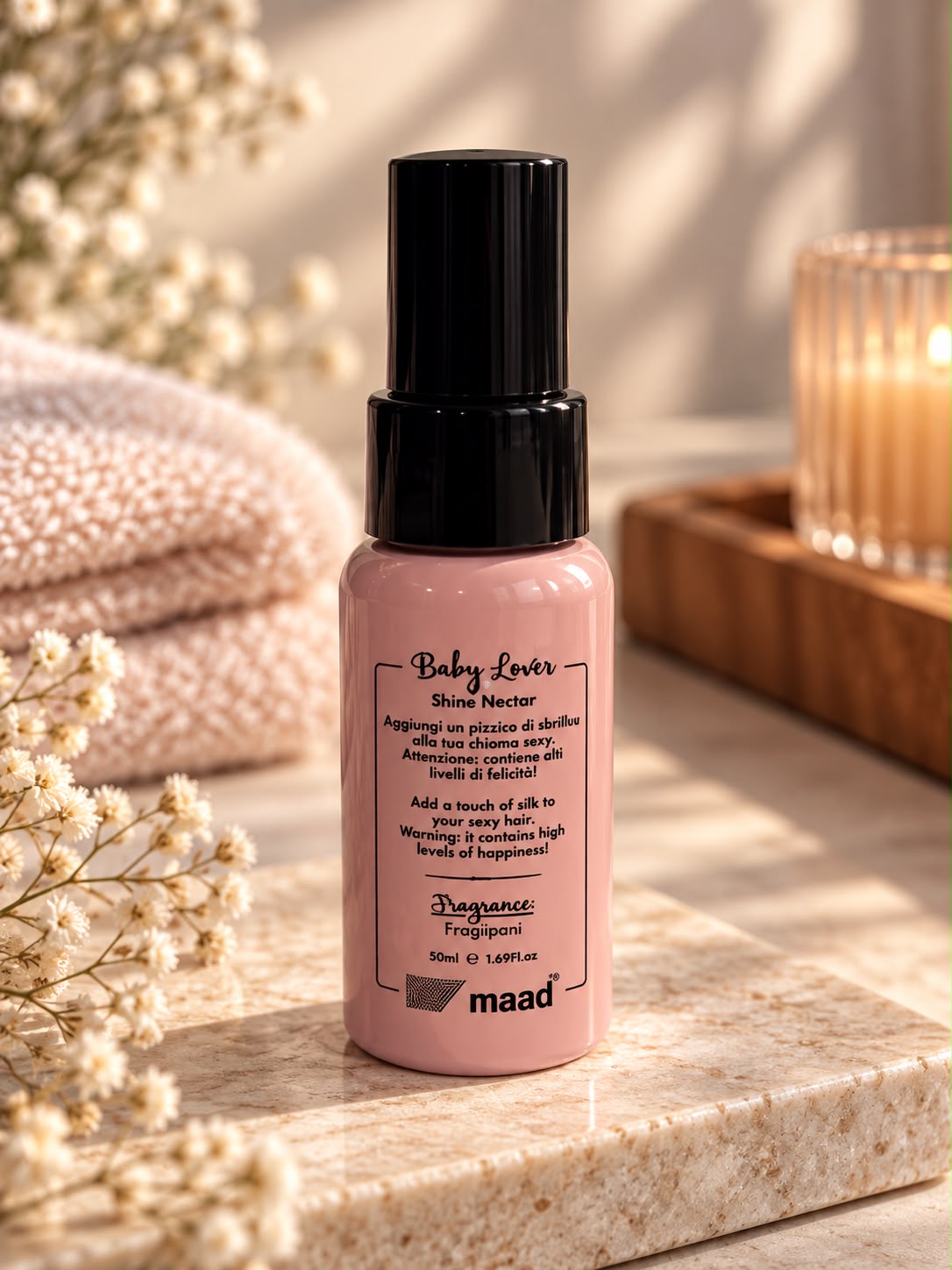 Pink bottle of maad Baby Lover Shine Nectar 50 ml on stone tray beside towels and flowers