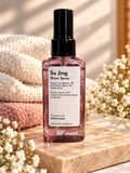 Pink 100 ml bottle of maad Su Jing Shine Spray beside folded towels and flowers